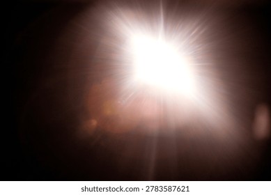 Bright light source radiates rays and flares in a dark setting, producing a striking illumination effect with visible light distortion and reflections