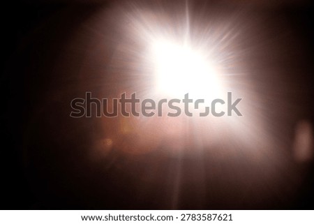 Bright light source radiates rays and flares in a dark setting, producing a striking illumination effect with visible light distortion and reflections