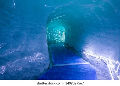 Bright lights illuminate the blue corridor carved into the ice of Mer De Glace. Beautiful blue ice tunnel leading through a mountain near Mont Blanc. Empty corridor leads through inside of a glacier.