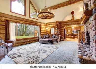 Bright Living Room Interior In American Log Cabin House. Rustic Chandelier, Stone Fireplace And High Ceiling With Wooden Beams Make Room Gorgeous. Northwest, USA