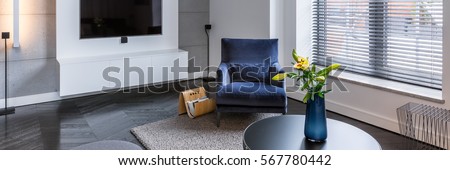 Bright living room with tv, blue armchair and round table, panorama