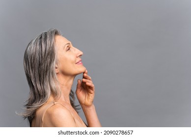 Bright Mature Lady Standing In Profile Looks Up, Touching Gently Chin Isolated On Gray Background, Side View At Senior Gray-haired Charming Lady, Elderly Beauty Female. Anti-aging Care Concept