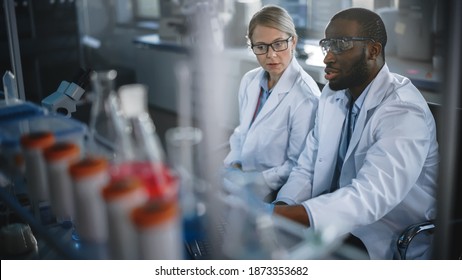 Bright Medical Science Laboratory with Diverse Team of Research Scientists Working. Young Female Microbiologist Talks to a Male Biochemist about New Test Results. High-Tech Equipment. - Powered by Shutterstock