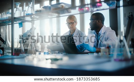 Bright Medical Science Laboratory with Diverse Team of Research Scientists Working. Young Female Microbiologist Talks to a Male Biochemist about New Good Test Results. High-Tech Equipment. ストックフォト © 