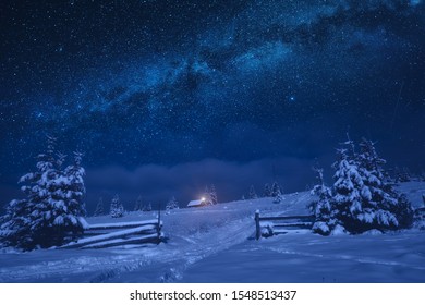 Bright Milky Way In A Night Starry Sky. Lonely House On A Snowy Hill With Christmas Light.