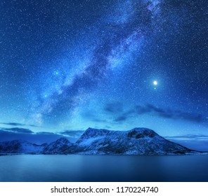 Bright Milky Way over snow covered mountains and sea at night in winter in Norway. Landscape with snowy rocks, starry sky, reflection in water, fjord. Lofoten Islands. Space. Beautiful milky way