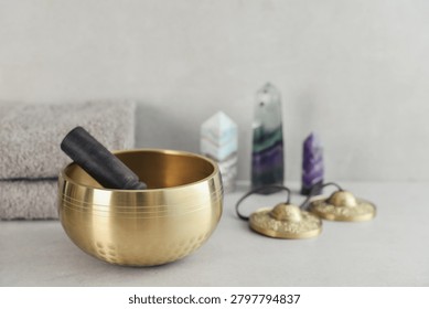 A bright, minimal wellness composition featuring a singing bowl surrounded by folded towels, tingsha bells, and healing crystals including amethyst, fluorite, and aragonite. 
