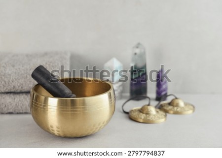 A bright, minimal wellness composition featuring a singing bowl surrounded by folded towels, tingsha bells, and healing crystals including amethyst, fluorite, and aragonite. 