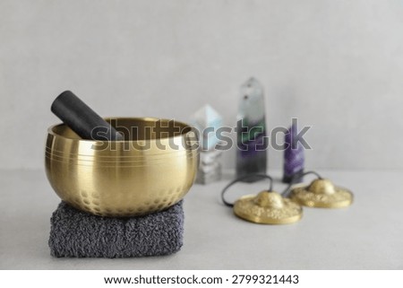 A bright, minimal wellness composition featuring a singing bowl surrounded by folded towels, tingsha bells, and healing crystals including amethyst, fluorite, and aragonite. 