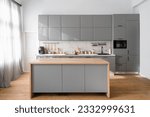 Bright minimalistic kitchen interior with gray furniture and big dining table on wooden floor. Cooking utensils and jars with food on countertop.