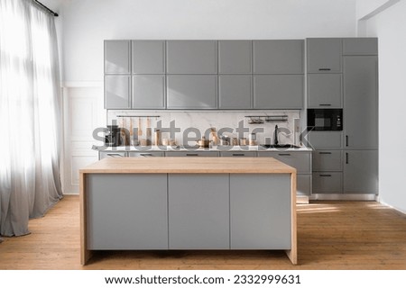 Bright minimalistic kitchen interior with gray furniture and big dining table on wooden floor. Cooking utensils and jars with food on countertop.