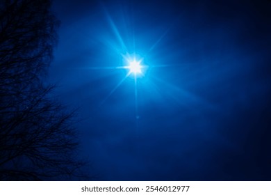 A bright moon casts a striking starburst effect in a deep blue night sky. Bare tree branches frame the scene on the left, adding a natural silhouette. - Powered by Shutterstock