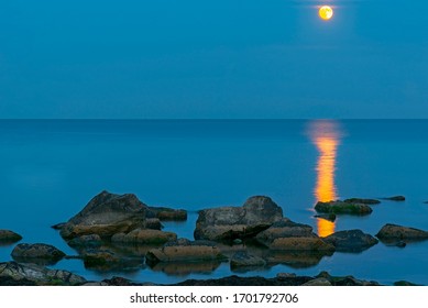 Bright moon over the sea in the night sky. Lunar path on the surface of the sea. 
Rock formations protrude from the water. - Powered by Shutterstock