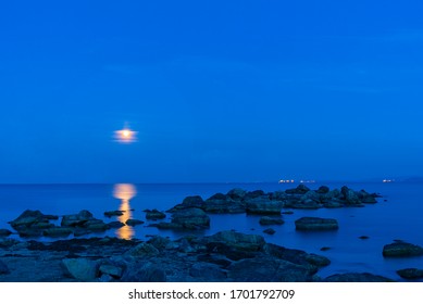 Bright moon over the sea in the night sky. Lunar path on the surface of the sea. 
Rock formations protrude from the water. - Powered by Shutterstock