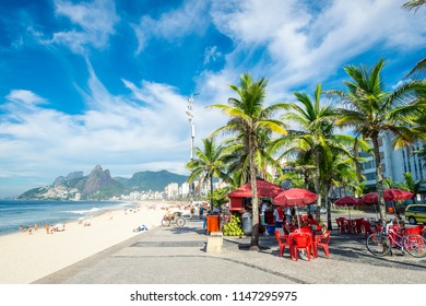 Bright Morning View Of A Kiosk And Palm Trees On The Ipanema Promenade With The Beach And Two Brothers Mountain Backdrop.