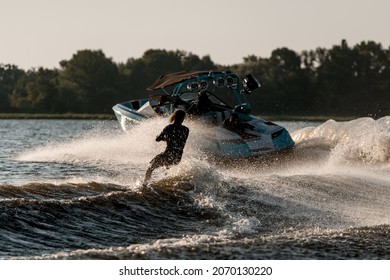 Bright motor boat pulls an active wet guy riding a wakeboard down the river Summertime watersports activity