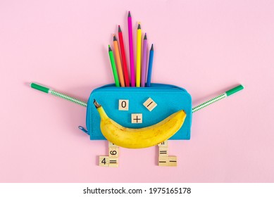 Bright multicolored school supplies, stationery and a banana in the form of a smiling character on a pink background. Back to school, preschool education. School lunch or breakfast. 