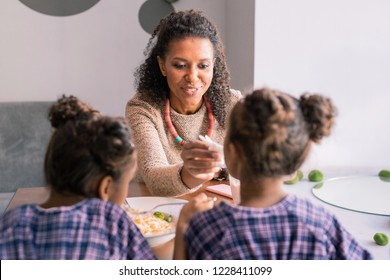 Bright Necklace. Curly Loving Mother Wearing Bright Necklace Giving Her Daughter Some Pasta