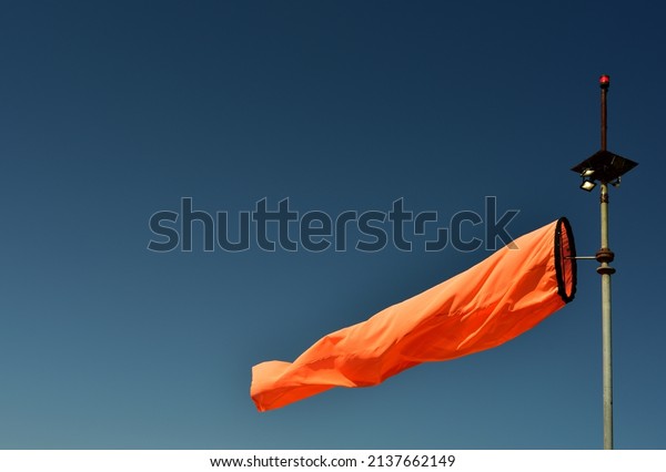 Bright neon orange wind sock blowing indicating\
wind direction against an azure\
sky