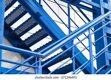 A Bright, New, Blue, Iron Fire Ladder. Diagonal Composition, Cross To The Cross. The Industrial Texture Is Shiny, With Glare Of The Sun In Pure White And Blue.