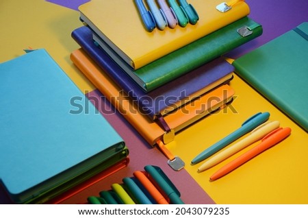 Bright notepads and colored pens on a background of colored paper. Writing accessories. Corporate gifts for office employees. Sunny mood for work.