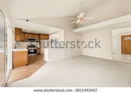 Bright, open-concept living space with white walls, cozy carpeting, vaulted ceilings, and a view into the kitchen featuring traditional wood cabinets