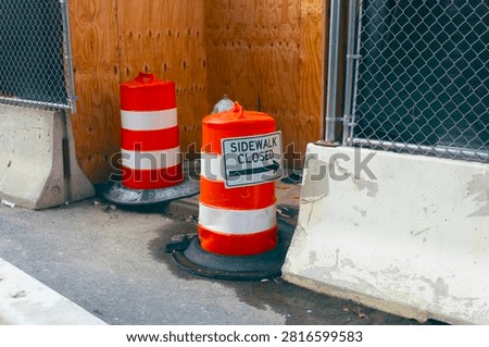 Bright orange construction barrels lining an urban street, representing road safety, ongoing city maintenance, and traffic management in an industrial setting.
