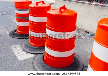 Bright orange construction barrels lining an urban street, representing road safety, ongoing city maintenance, and traffic management in an industrial setting.

