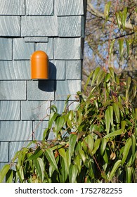 A Bright Orange Dome-shaped Metal Sconce Brings A Mid-century Modern Touch To The Exterior Of A House With Painted Cedar Siding. A Deep Green Climbing Vine Softens The Corner.