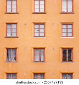 Bright orange facade of an apartment building displays symmetrical wooden framed windows, showcasing minimalist and urban architecture. Ideal for projects focusing on city living or vibrant decor. - Powered by Shutterstock