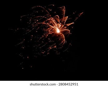 Bright orange firework explosion creating glowing light trails against a dark black night sky.