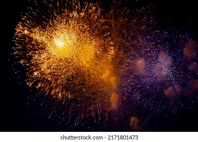 A bright orange firework and next to it a blue firework with sparks on the background of the night sky. High quality photo