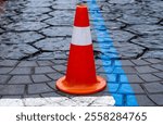 Bright orange road cone stands on the asphalt road, marking caution for traffic and ensuring safety in a busy urban environment