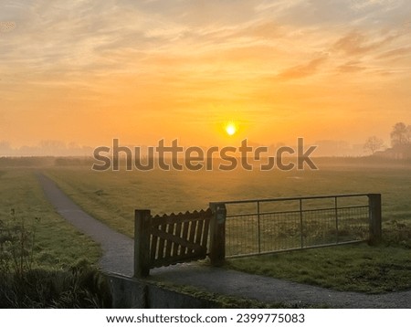 Bright orange sunrise at fields with light fog and a fence or gate in Holland. High quality photo
