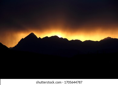 A bright orange sunset over sharp black Pamir mountains in the shade