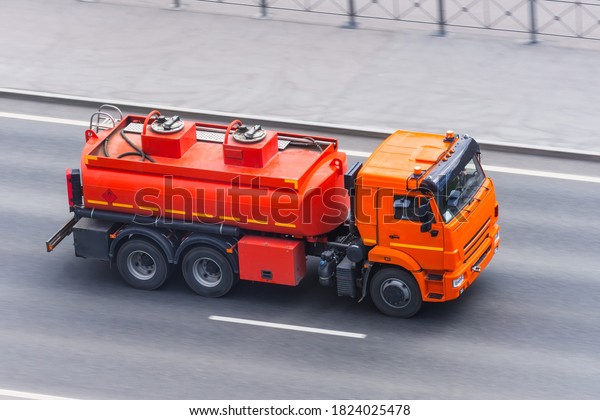 A bright\
orange truck with a tank for combustible fuel and other flammable\
liquids is driving along the\
highway