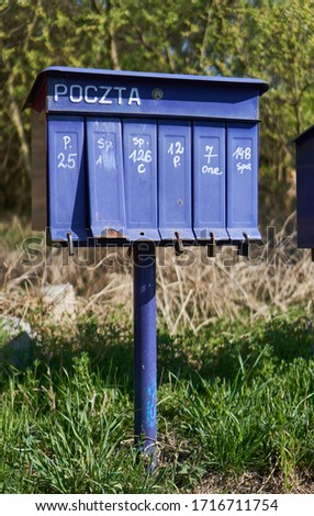 Bright outdoor cluster mailboxes with individual slots in rural Poland. The text in Polish on the mailbox translates to: 'The post office of Poland'                               
