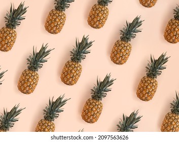 A bright pattern of many pineapples on a trendy soft beige pink background. Tropical ripe juicy fruit flat lay for your design projects
