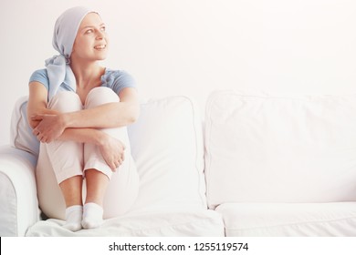 Bright photo of happy pretty girl suffering from kidney cancer, wearing blue headscarf and siting on the couch at hospice after chemotherapy