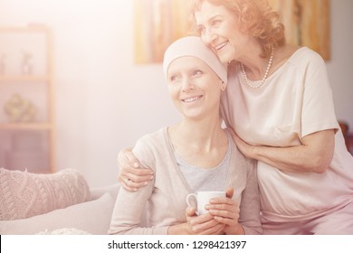 Bright photo of two positive senior woman sitting together at home enjoining their time after cancer treatment - Shutterstock ID 1298421397