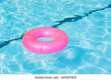 Bright Pink Float In Blue Swimming Pool, Ring Floating In A Refreshing Blue Swimming Pool With Waves Reflecting In The Summer Sun. Active Vacation Background. Lifesaver For Kid. Sunny Day At The Pool.