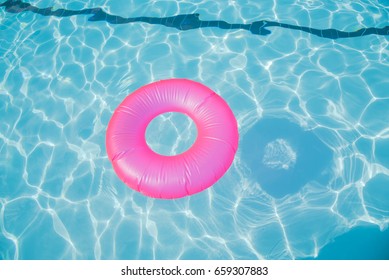 Bright pink float in blue swimming pool, ring floating in a refreshing blue swimming pool with waves reflecting in the summer sun. Active vacation background. Lifesaver for kid. Sunny day at the pool.