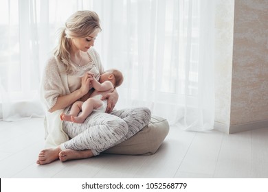 Bright portrait of a mom breast feeding baby over window lighting.