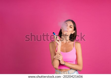Bright portrait of young beautiful woman on pink background smoking electronic cigarette, enjoying, a lot of smoke