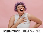 Bright positive girl with purple short wavy hair in white outfit and earrings with pierced nose laughs on pink background..