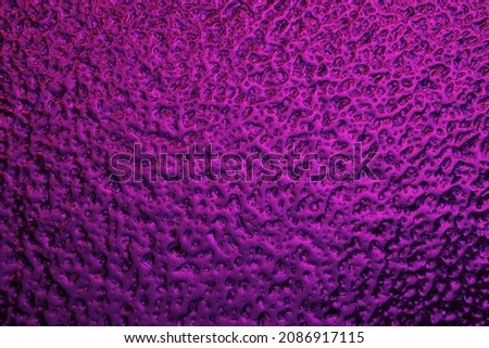 Bright purple winter background. The surface of ice frozen on the window pane. An abstract pattern with a metallic sheen, similar to the ripples of mercury. Rich violet wallpaper. Close-up