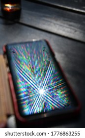 Bright Rainbow Rays Reflect In Mobile Phone Screen Surface With Blurred Background. Multicolored Beams And Reflection Atop Smartphone Screen Closeup