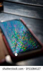 Bright Rainbow Rays Reflect In Mobile Phone Screen Surface With Dark Blurred Background. Multicolored Beams And Reflection In Smartphone Screen Closeup