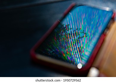 Bright Rainbow Rays Reflect In Mobile Phone Screen Surface With Dark Blurred Background. Multicolored Beams And Reflection In Smartphone Screen Closeup