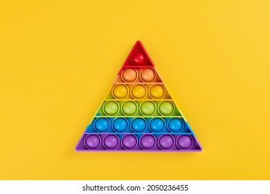 Bright rainbow toy antistress for children and adults on a yellow background. Flexible sensory antistress toy pop it triangle shape